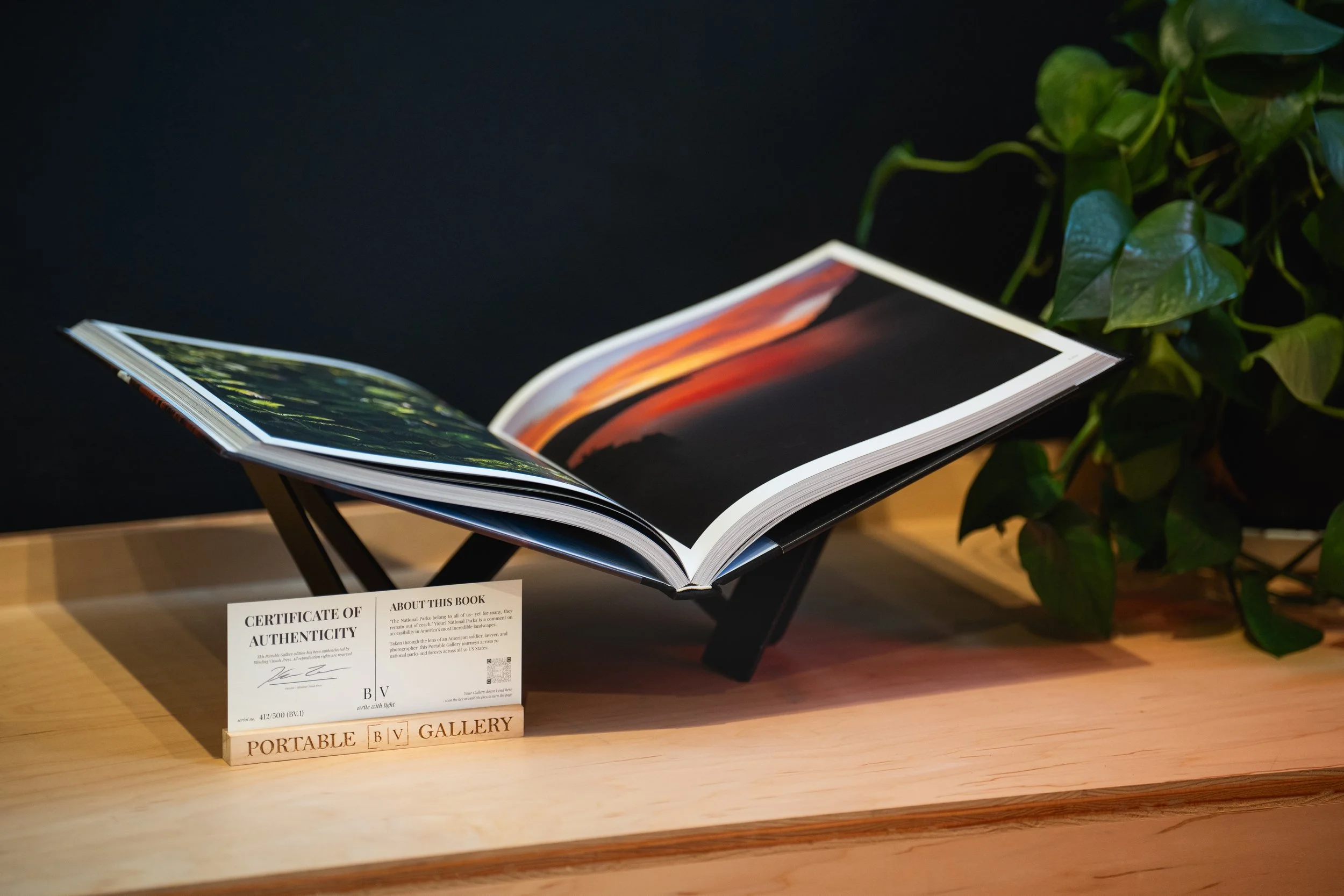 An open photo book on a wooden stand beside its certificate of authenticity